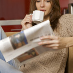 Mid adult woman drinking coffee and reading news